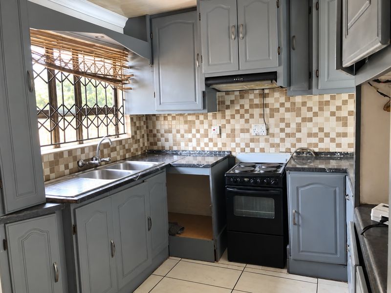 A functional kitchen featuring grey cabinetry, a double bowl sink, tiled backsplash, and a freestanding stove with an integrated extractor fan.