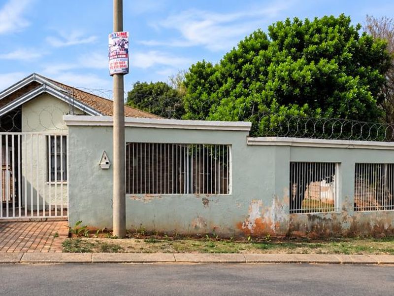 Front exterior view of the property featuring a perimeter wall with security fencing, a gated driveway, and metal security bars on windows.
