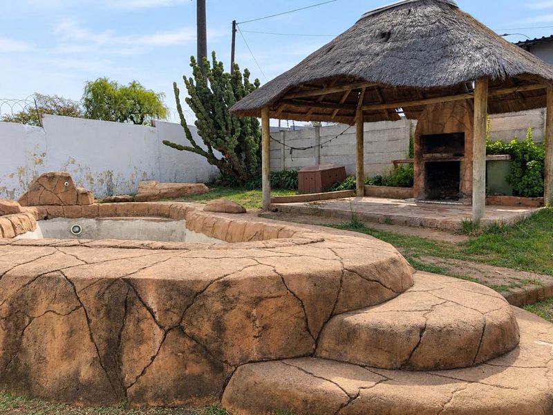 Outdoor entertainment area featuring a rock-style swimming pool and a thatched lapa with a built-in braai, set within a walled garden.