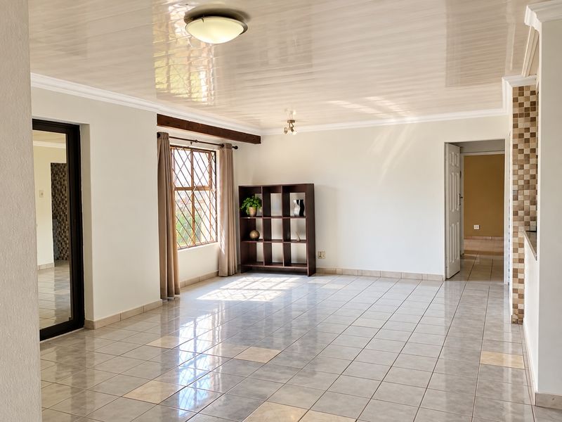 A spacious, light-filled living area featuring neutral tiled flooring, a glossy ceiling finish, and a decorative mosaic tile pillar.