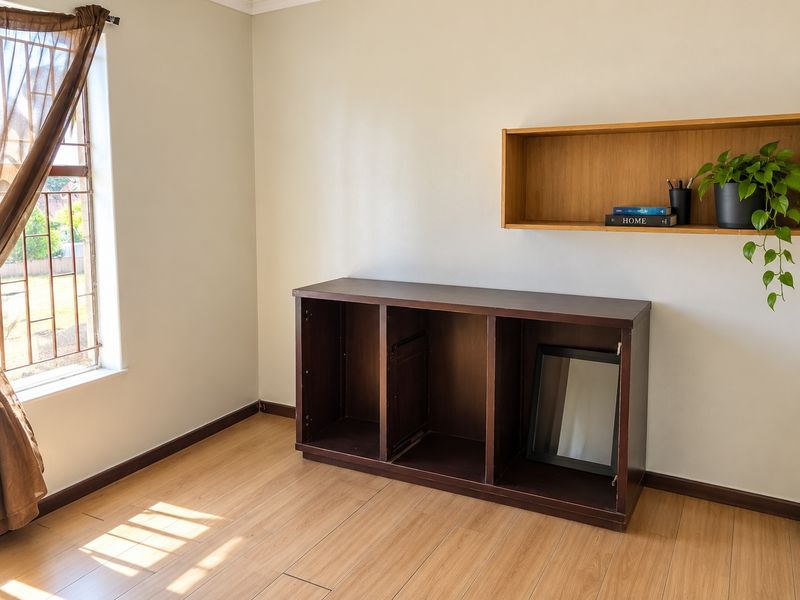 A bedroom featuring light laminate flooring, a window with security bars, and built-in wall shelving.