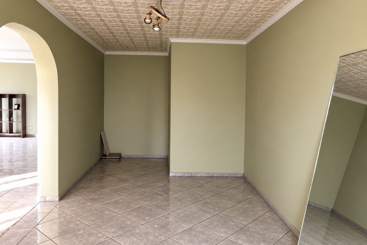 An empty living room featuring tiled flooring, a textured ceiling, and an arched entryway leading to an adjacent space.