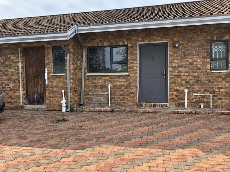 Front exterior view of a face brick house featuring a paved driveway, tiled roof, and multiple entry points with aluminium window frames.