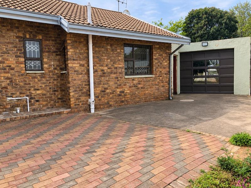 Exterior view of a face brick house featuring a paved driveway, tiled roof, and an attached garage with a sectional door.