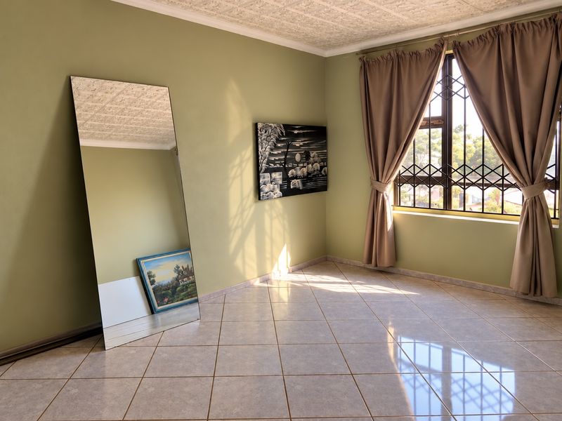 A bright, empty bedroom featuring tiled flooring, a textured ceiling, and a window fitted with a security gate.