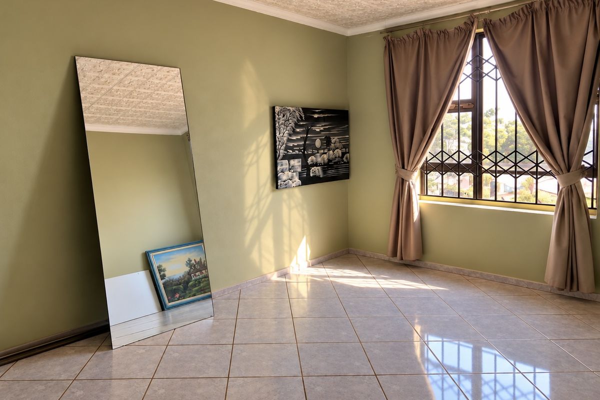 A bright, empty bedroom featuring tiled flooring, a textured ceiling, and a window fitted with a security gate.