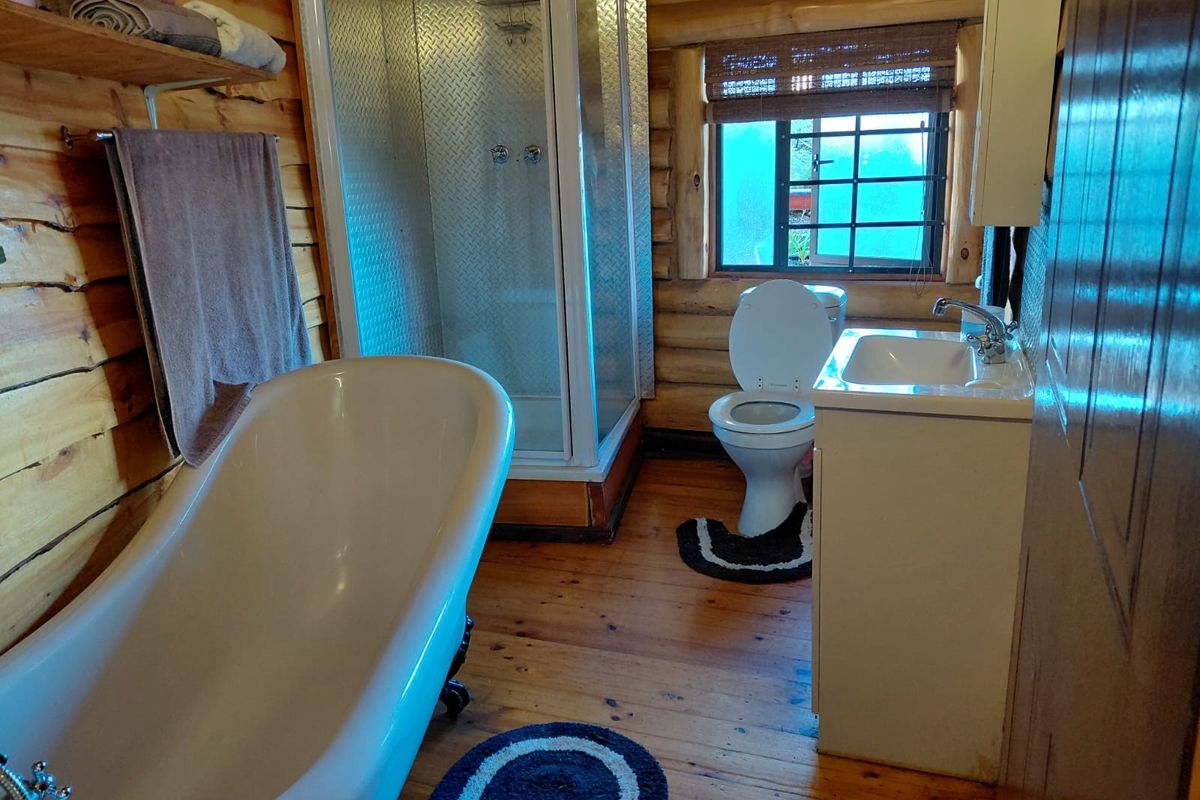Rustic bathroom featuring timber log walls, timber flooring, a freestanding bathtub, a separate shower enclosure, and a vanity basin.