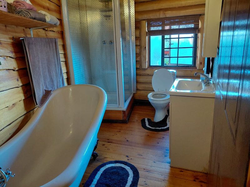 Rustic bathroom featuring timber log walls, timber flooring, a freestanding bathtub, a separate shower enclosure, and a vanity basin.