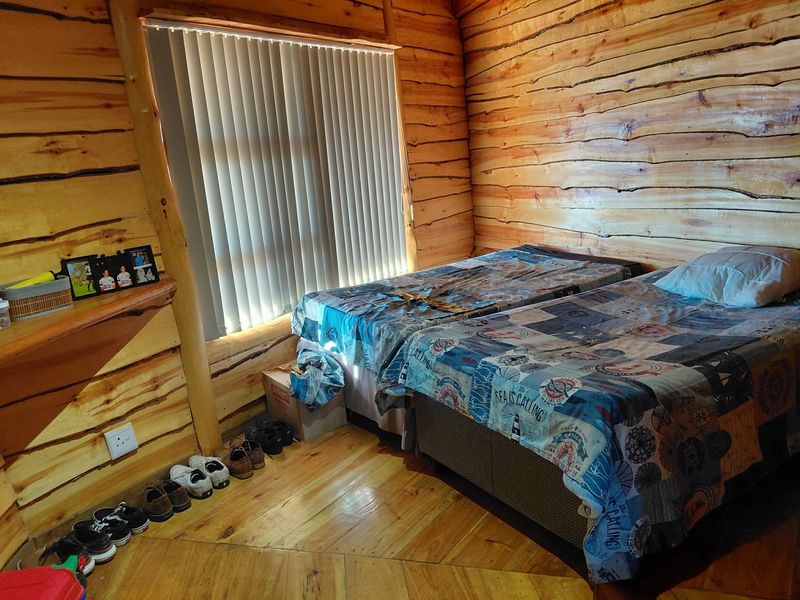 A rustic bedroom featuring natural log walls, timber flooring, and vertical window blinds.
