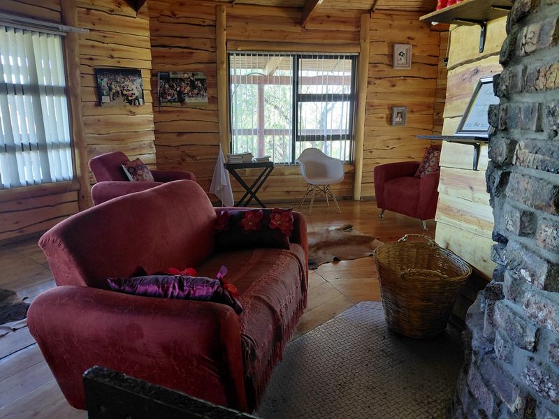 Rustic living room featuring exposed log walls, timber flooring, and a prominent stone fireplace.
