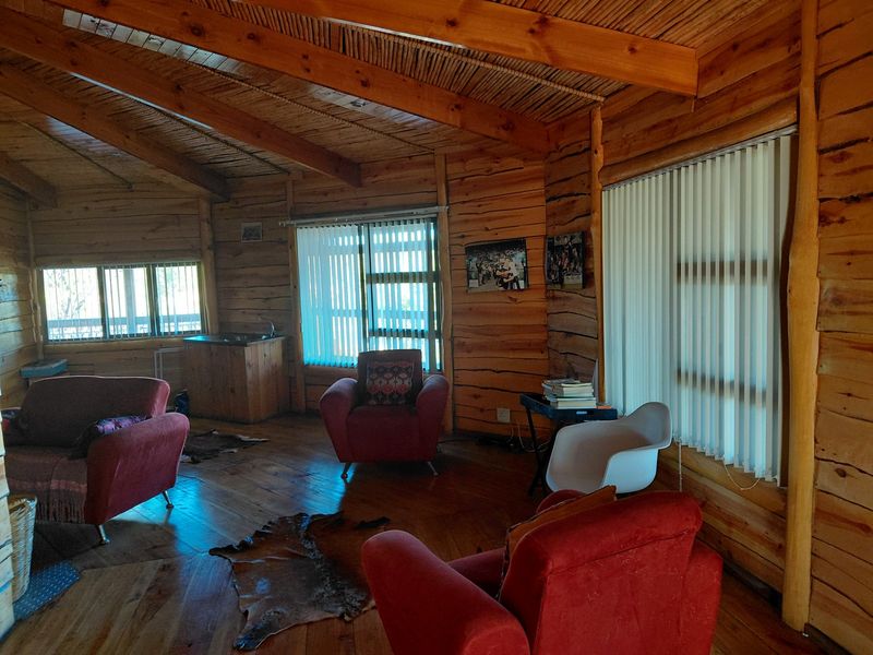 Spacious living area featuring rustic exposed log walls, timber beam ceiling with thatch detailing, and warm timber flooring throughout.