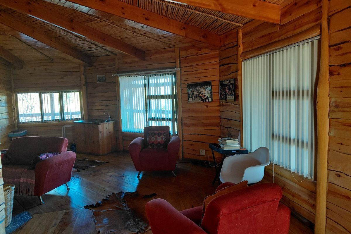 Spacious living area featuring rustic exposed log walls, timber beam ceiling with thatch detailing, and warm timber flooring throughout.