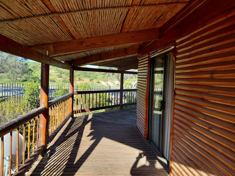 A spacious wooden balcony featuring timber decking, a bamboo-lined roof, and a log-style exterior wall, offering an open outdoor living space.