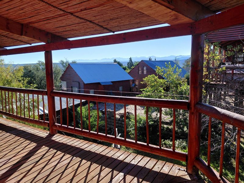 A covered timber balcony featuring a rustic wooden railing and deck, offering elevated views of the surrounding property and distant mountain landscape.