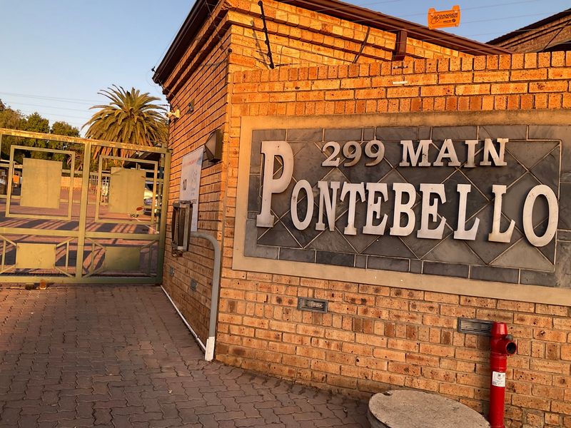 Entrance view of the Pontebello apartment complex featuring a brick facade, secure metal gate, and paved driveway access.