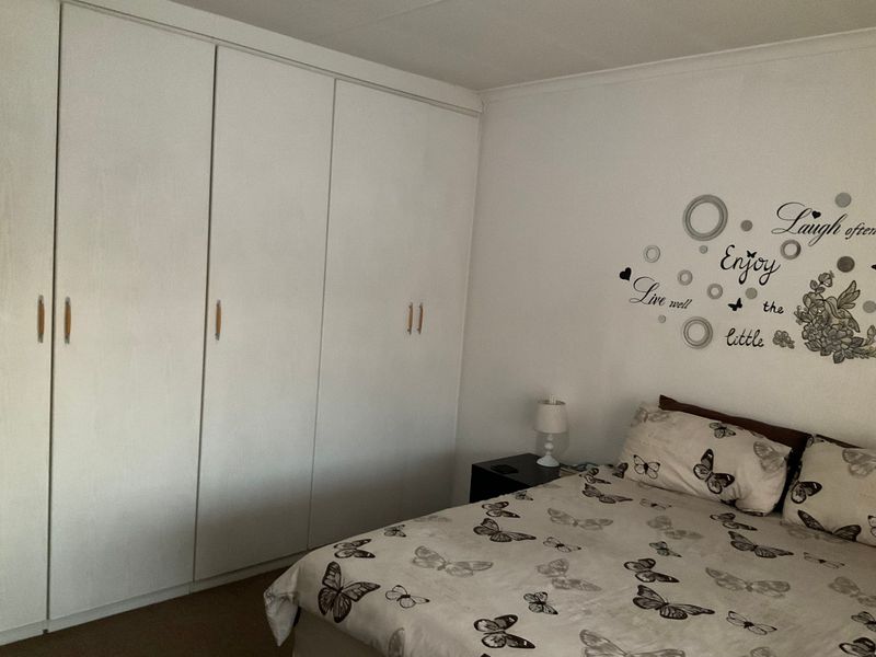 A bedroom featuring a large white built-in wardrobe with ample storage space.