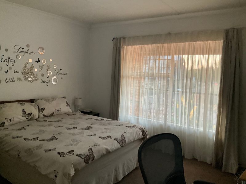 A bedroom featuring natural light through a large window with installed security bars and curtain rails.