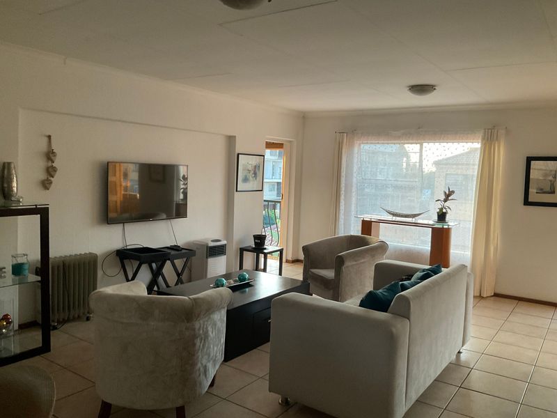 A spacious living room featuring tiled flooring, large windows for natural light, and direct access to an outdoor balcony area.