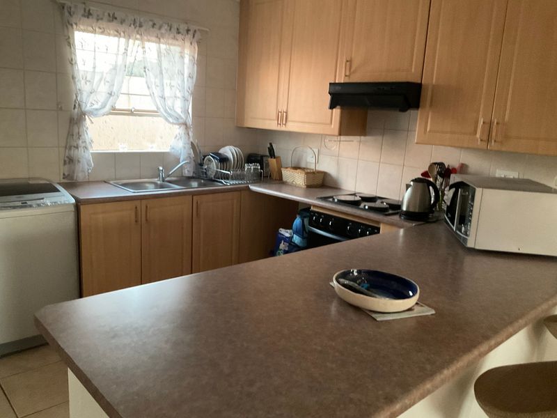 A functional kitchen featuring light wood-finish cabinetry, laminate countertops, a double basin sink, and built-in cooking appliances with a tiled backsplash.
