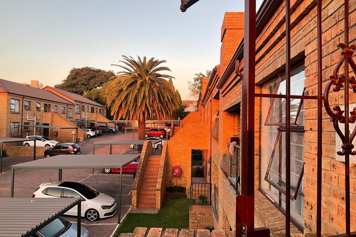 View of the apartment complex exterior featuring brick facade, paved parking area with carports, and communal outdoor spaces at sunset.