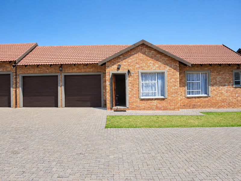 Front elevation of a brick townhouse featuring a double garage, paved driveway, and well-maintained exterior finishes under a clear blue sky.