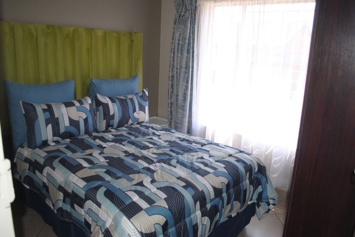 A compact bedroom featuring tiled flooring and a built-in cupboard, with natural light entering through a window dressed with curtains.