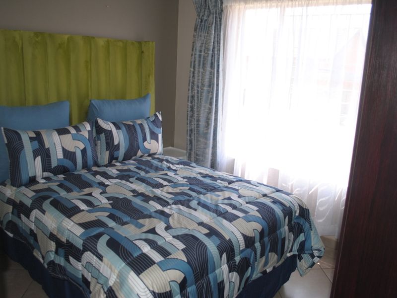 A compact bedroom featuring tiled flooring and a built-in cupboard, with natural light entering through a window dressed with curtains.