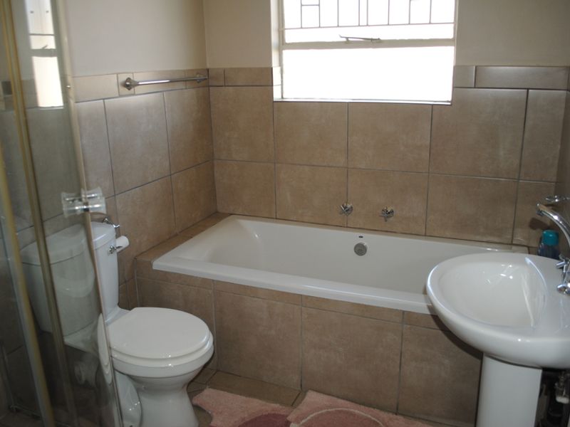 A functional bathroom featuring a bathtub, pedestal basin, toilet, and a separate shower enclosure with neutral wall tiling.