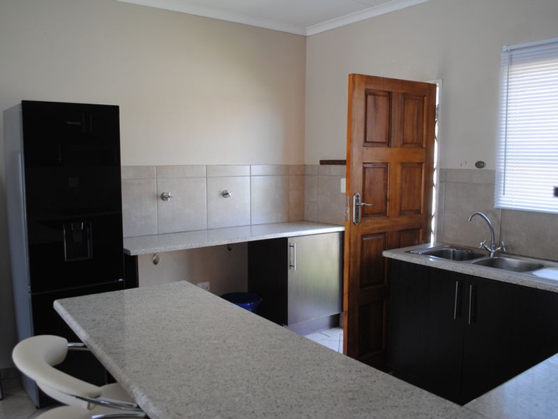 A functional kitchen featuring granite countertops, dark cabinetry, a double basin sink, and tiled splashbacks with direct access to an exterior door.