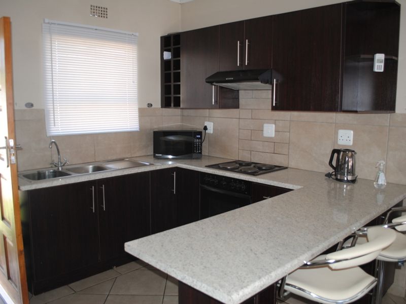 Functional kitchen featuring dark wood cabinetry, granite countertops, breakfast bar, built-in oven, and hob with a tiled backsplash and natural light.