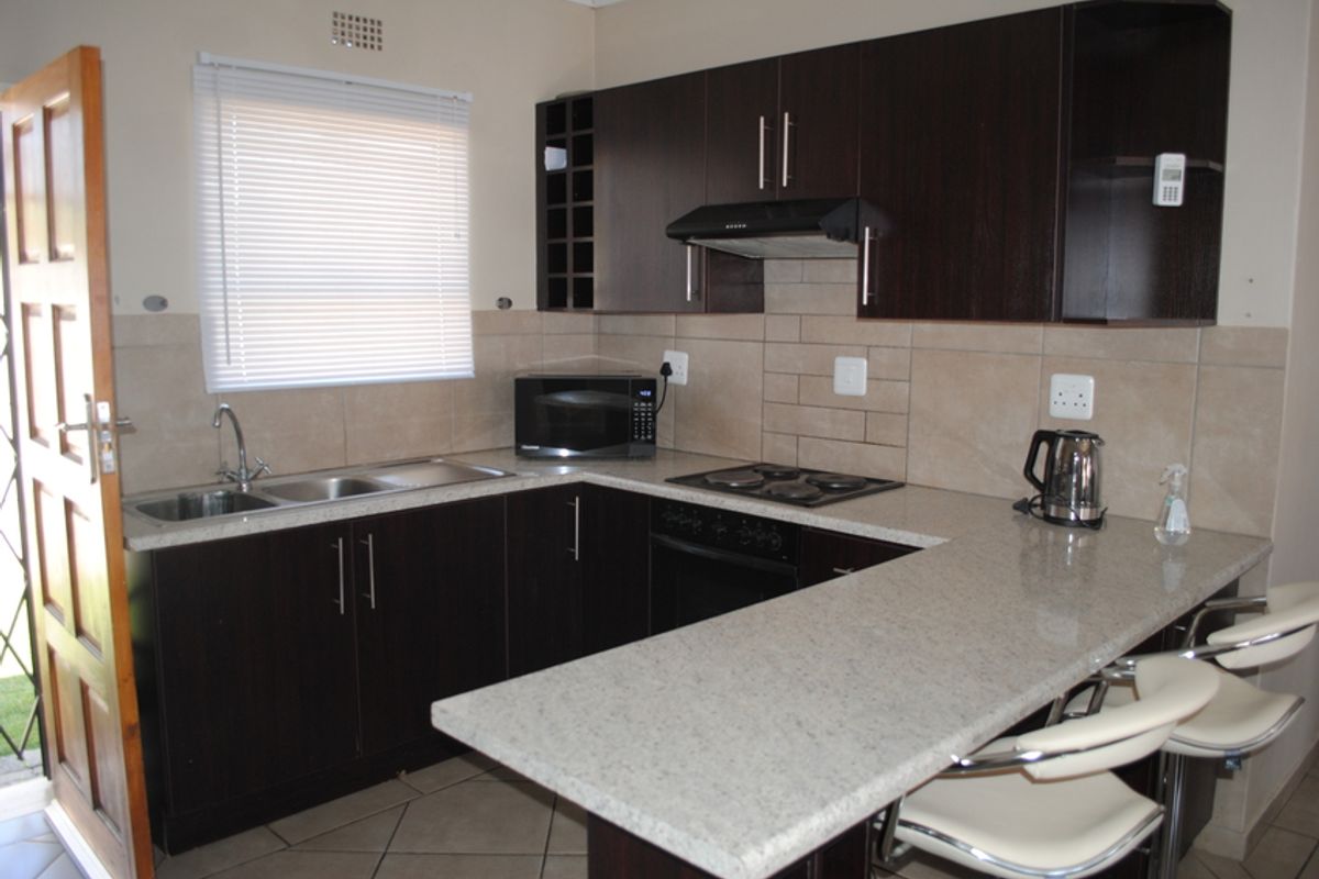 Functional kitchen featuring dark wood cabinetry, granite countertops, breakfast bar, built-in oven, and hob with a tiled backsplash and natural light.