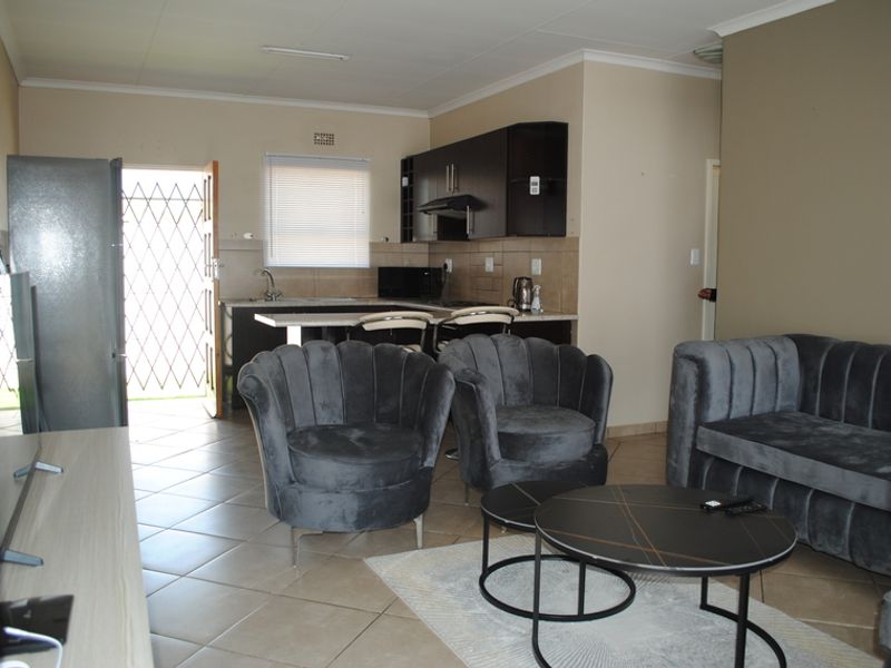 Open plan living area featuring a compact kitchen with dark cabinetry, tiled flooring throughout, and direct access to an exterior security gate.