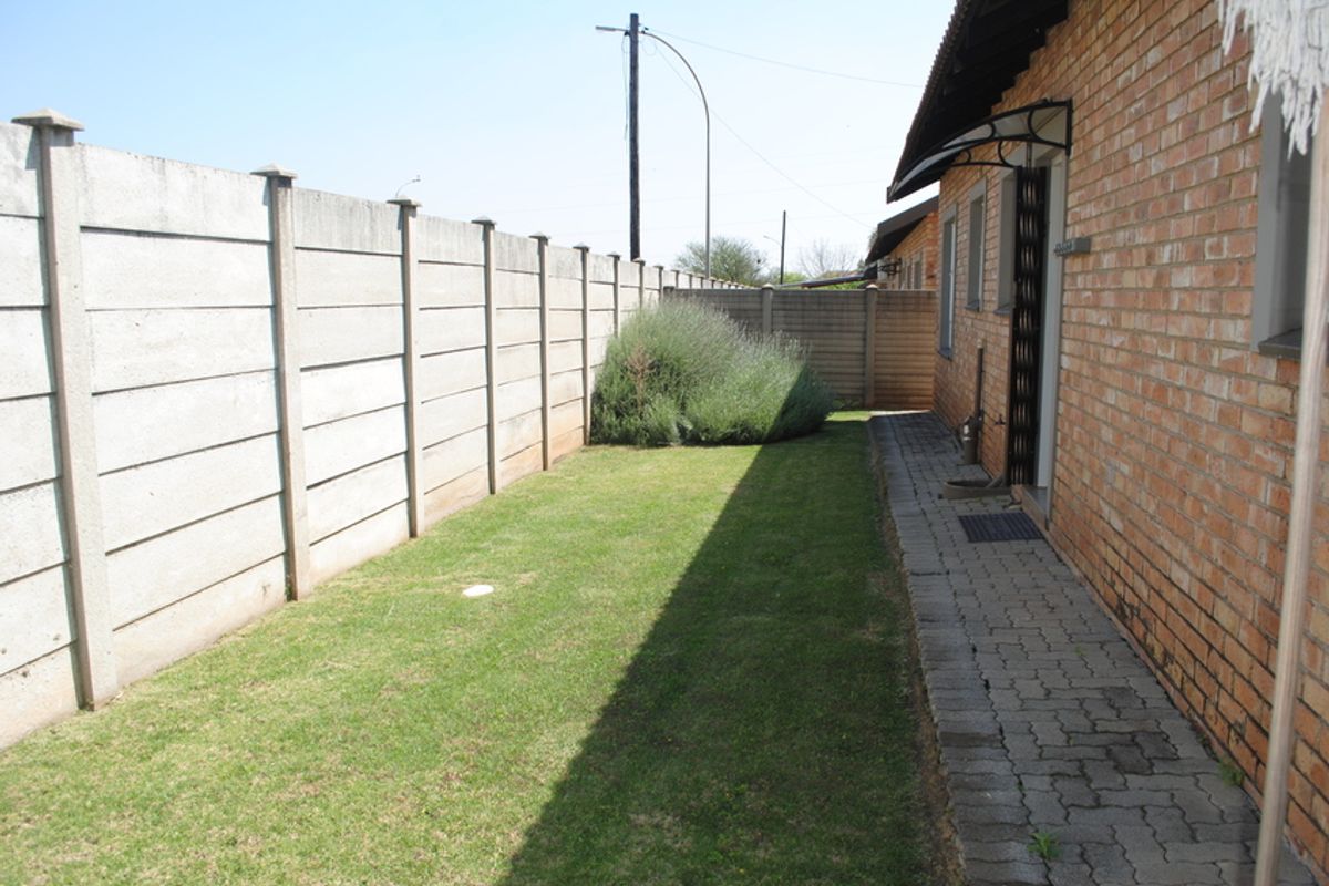 A private rear garden area featuring a paved walkway, brick exterior wall, and a precast concrete boundary fence.