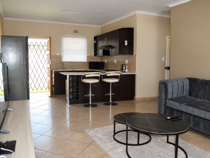 Open-plan living area featuring a modern kitchen with dark cabinetry, a breakfast island, and tiled flooring, leading directly to an exterior security gate.