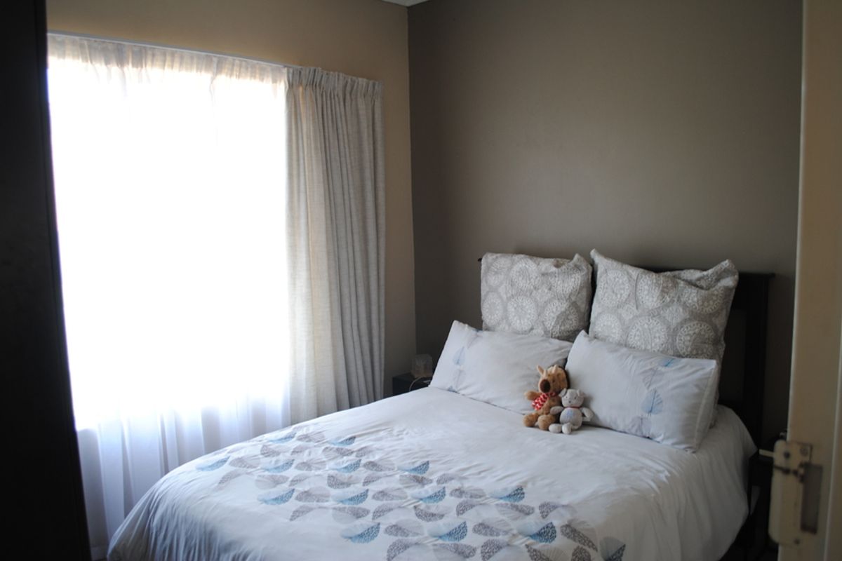 A cozy bedroom featuring neutral wall tones and natural light through a window with installed curtain tracks.