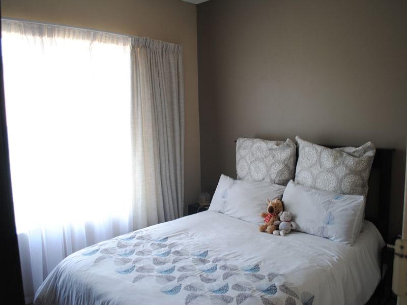 A cozy bedroom featuring neutral wall tones and natural light through a window with installed curtain tracks.
