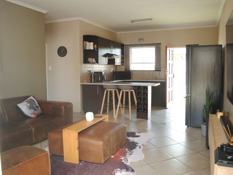 Open-plan living area featuring a functional kitchen with built-in cabinetry, breakfast counter, and tiled flooring, seamlessly connecting to the lounge space.