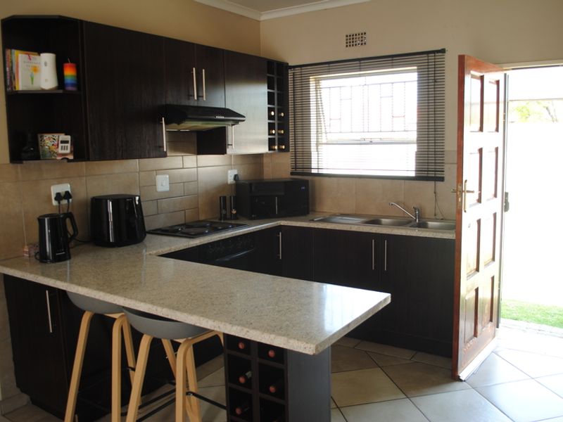 A functional kitchen featuring dark wood cabinetry, stone-look countertops, a breakfast bar, built-in hob, extractor fan, and direct access to the exterior.