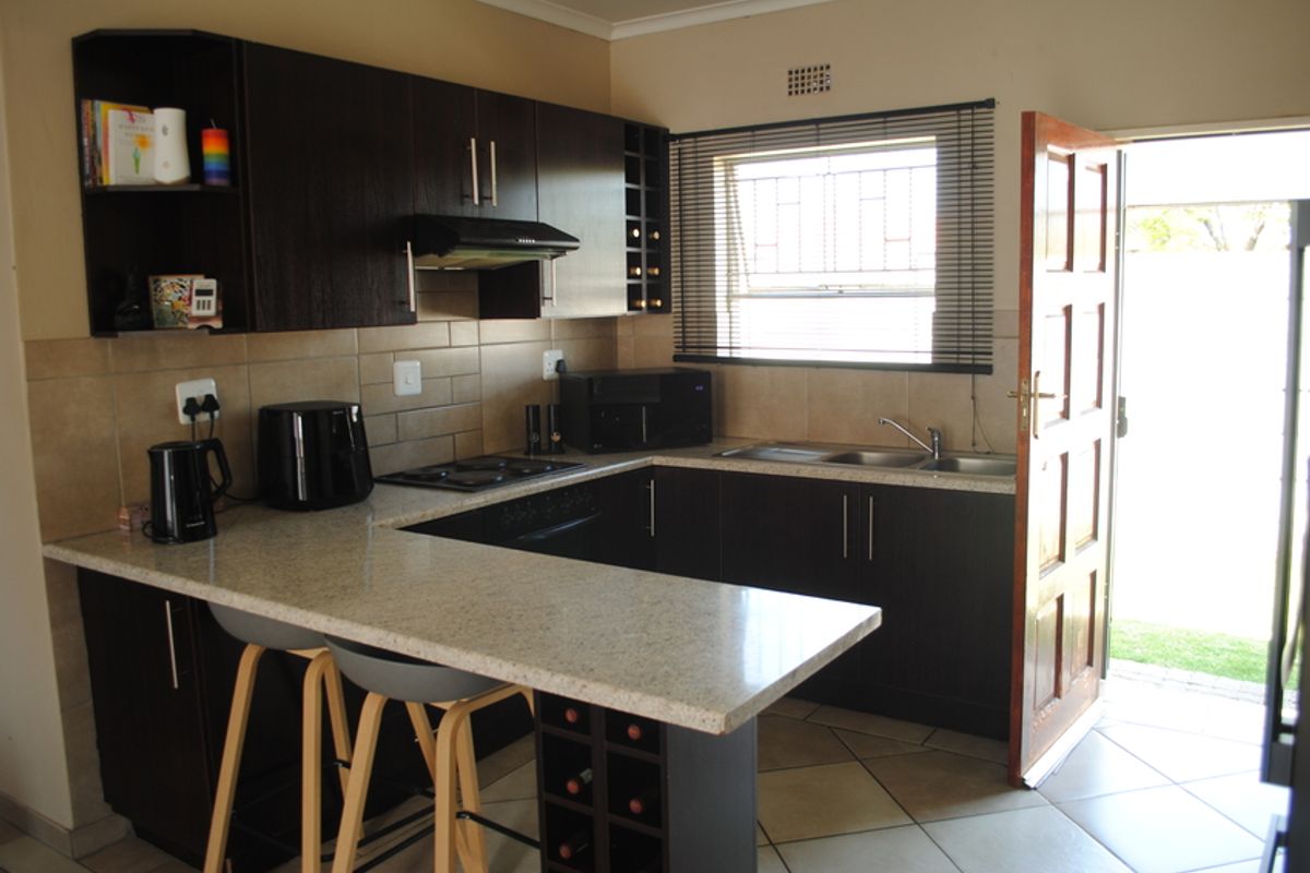 A functional kitchen featuring dark wood cabinetry, stone-look countertops, a breakfast bar, built-in hob, extractor fan, and direct access to the exterior.