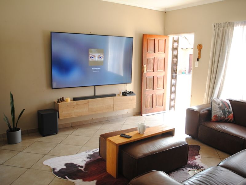 A comfortable living room featuring tiled flooring, wall-mounted cabinetry, and direct access to the exterior through a timber door with a security gate.