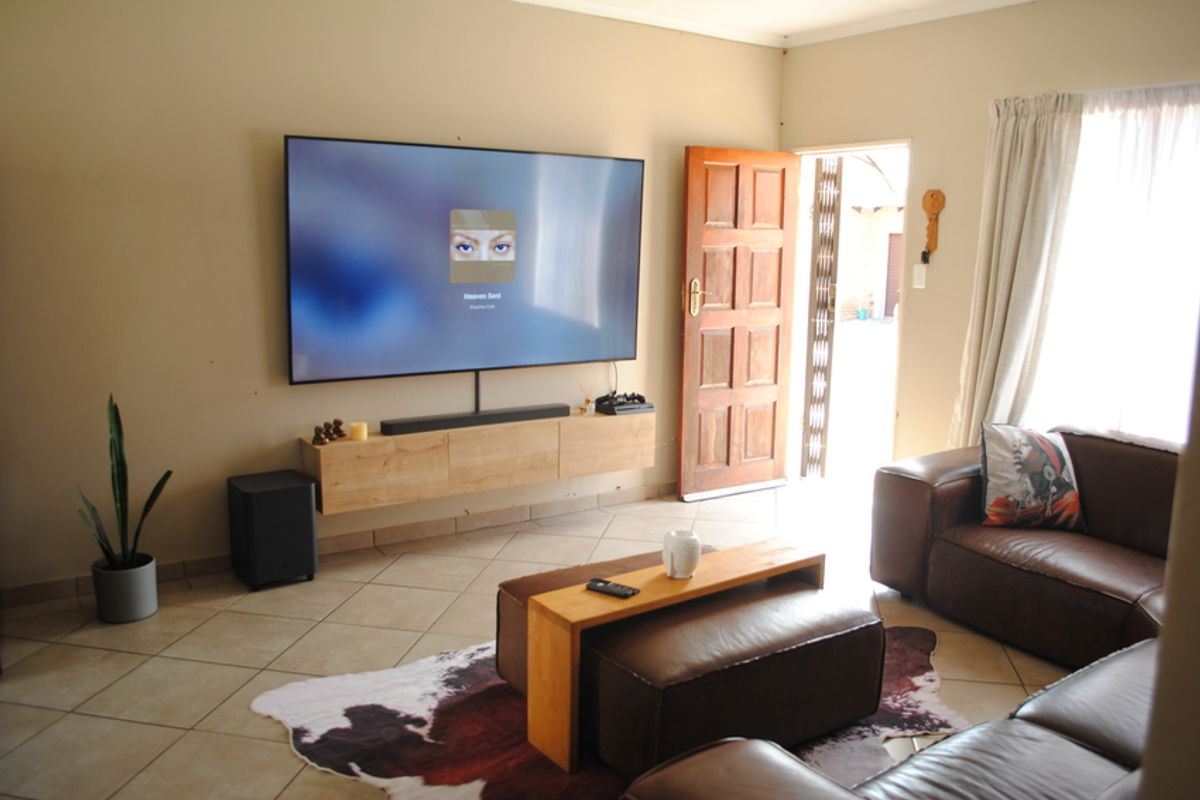 A comfortable living room featuring tiled flooring, wall-mounted cabinetry, and direct access to the exterior through a timber door with a security gate.