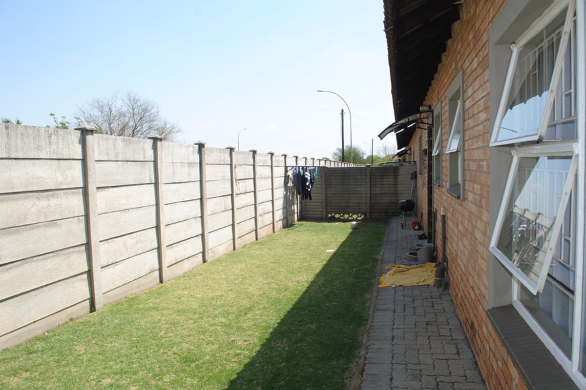 Rear exterior view of the townhouse featuring a brick facade, paved walkway, and a private garden enclosed by a precast concrete boundary wall.