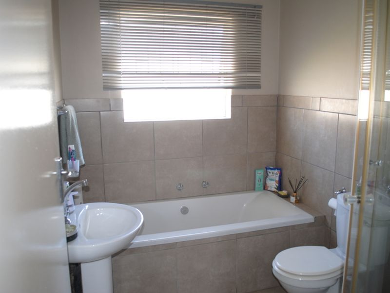 A functional bathroom featuring a pedestal basin, built-in bathtub, separate shower enclosure, and neutral wall tiling with venetian blinds for privacy.