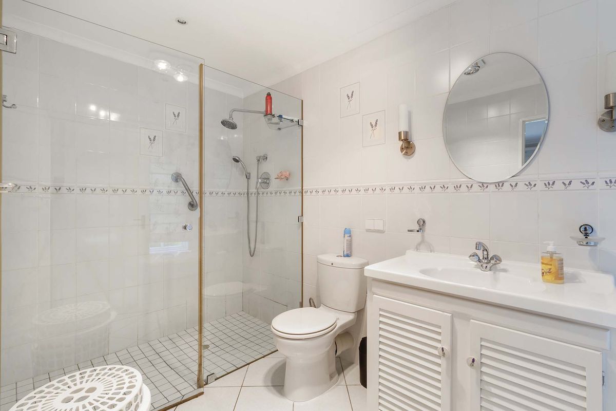 A functional bathroom featuring a walk-in shower with glass enclosure, a white vanity cabinet with basin, and a wall-mounted mirror.