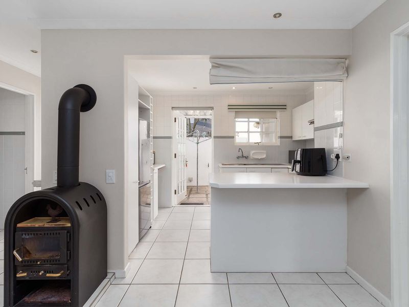 Open plan living area featuring a freestanding fireplace, tiled flooring, and a functional kitchen with a breakfast counter and direct access to the rear exterior.