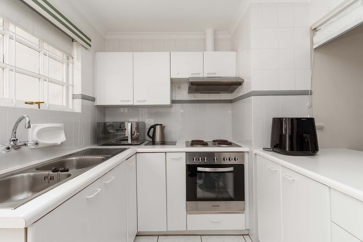 A compact, functional kitchen featuring white cabinetry, a stainless steel double sink, built-in oven, electric hob, and tiled splashback.