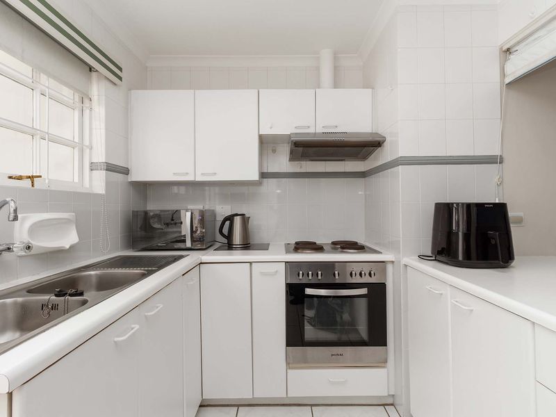 A compact, functional kitchen featuring white cabinetry, a stainless steel double sink, built-in oven, electric hob, and tiled splashback.