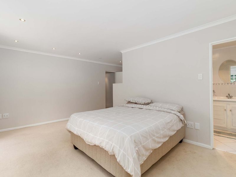 A spacious bedroom featuring neutral walls, recessed downlighting, and an adjoining en-suite bathroom with a vanity unit.