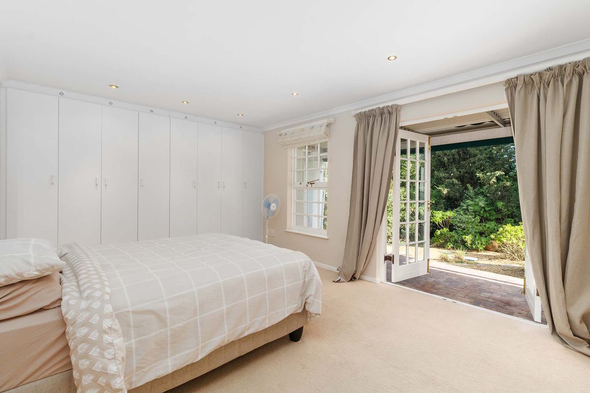 Spacious bedroom featuring extensive built-in cupboards, recessed lighting, and direct access to a private patio through classic French doors.