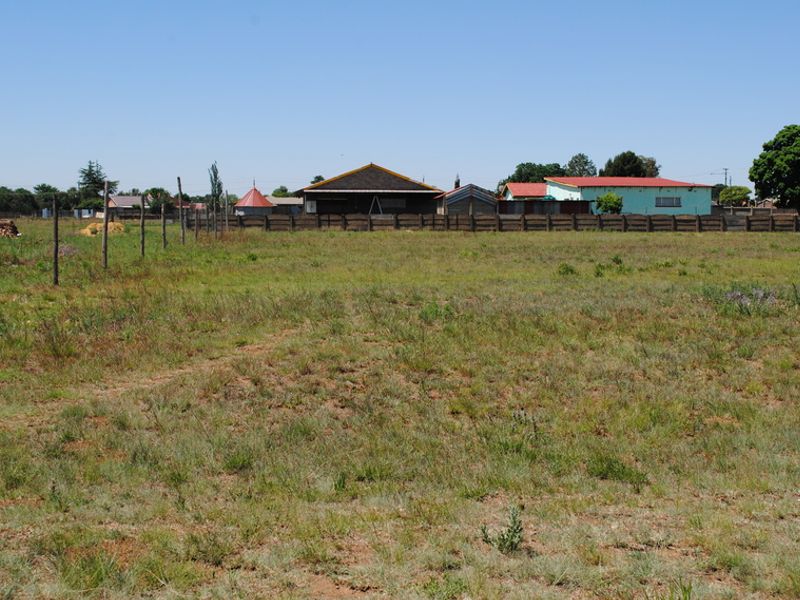 A view of a vacant residential plot featuring open grass land and perimeter fencing.